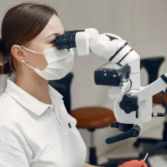 Dentystka w masce i rękawiczkach wykonuje leczenie kanałowe zęba krok po kroku, używając mikroskopu.