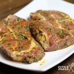 Zwei saftige Steaks, mariniert mit Kräutern und Gewürzen, liegen auf einem weißen Teller. Die Frage: Steak marinieren oder nicht?
