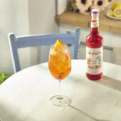 Orzeźwiający aperitif spritz z syropem Monin Orange Spritz, lodem i plasterkiem pomarańczy.