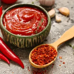 Miseczka pełna pikantnego sosu meksykańskiego, obok świeże papryczki chili i łyżka płatków chili.