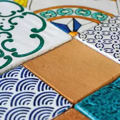 Composizione di mattonelle fai da te con decori geometrici e floreali in blu, verde e giallo, alternate a tasselli color sabbia e turchese.