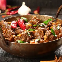 Aromatyczny gulasz z jagnięciny w miedzianym naczyniu, ozdobiony papryczkami chili i liśćmi curry.