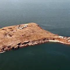 Wyspa Węży, skalista, sucha, z kilkoma budynkami i latarnią morską, otoczona ciemnym morzem.