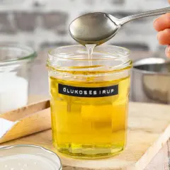 Glas mit Glukosesirup, bereit für leckere glucose rezepte. Daneben Zucker und ein Schneebesen.