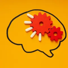Czerwone trybiki i białe kapsułki symbolizują działanie psychobiotyku na mózg, poprawiając jego funkcjonowanie.