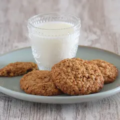 Un vaso de leche acompaña a unas deliciosas galletas de avena sobre un plato.