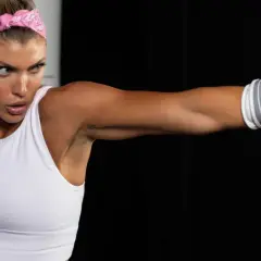Woman in white sports bra and pink bandana throws a punch, her glove about to fade back from the impact.