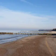 Spokojna plaża w Rusinowie z drewnianymi falochronami. Idealne miejsce na relaks i podziwianie widoków.