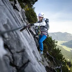 Uśmiechnięta kobieta na via ferrata dla początkujących, z widokiem na dolinę.