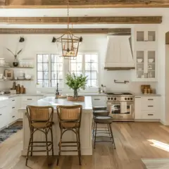 Jasna kuchnia w stylu modern farmhouse z drewnianymi belkami, wyspą i rattanowymi hokerami.
