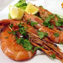 Gamberoni in padella succulenti, guarniti con prezzemolo fresco e spicchi di limone, pronti per essere gustati.