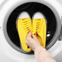 Ręka wkłada żółte trampki do otwartej suszarki bębnowej.
