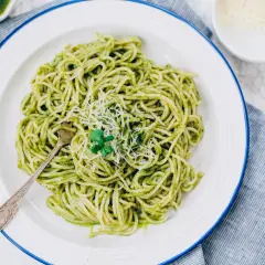 Porcja spaghetti z zielonym pesto, posypana parmezanem, na białym talerzu.