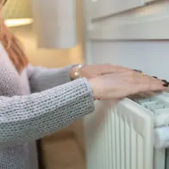 Dłonie na zimnych grzejnikach po odpowietrzeniu. Kobieta w swetrze sprawdza, czy ogrzewanie działa.