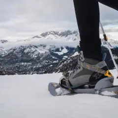 Persona camina con raquetas de nieve sobre un paisaje montañoso nevado. Hay varios tipos de raquetas de nieve.