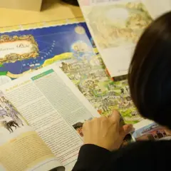 Osoba przegląda książkę z mapą Polski i ilustracjami mitologicznymi.