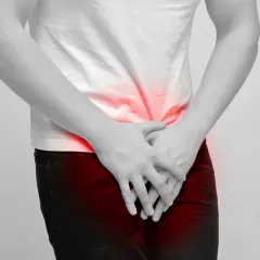 Mężczyzna trzyma ręce na podbrzuszu, gdzie widoczne są czerwone plamy bólu. Może to symbolizować dyskomfort związany z masowaniem prostaty.