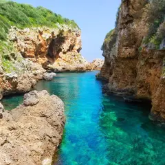 Magnifique paysage minorquin : criques rocheuses aux eaux turquoise cristallines, végétation luxuriante sur les falaises.