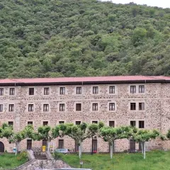 Edificio de piedra con tejado rojo, rodeado de árboles y un monte frondoso. Es el monasterio de Santo Toribio de Liébana.