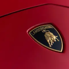 Złote logo Lamborghini z bykiem na czerwonym tle samochodu.
