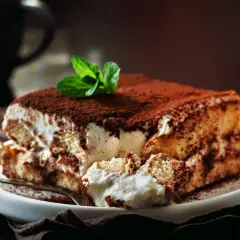 Pyszne tiramisu bez jajek, posypane kakao i udekorowane listkiem mięty, czeka na widelcu.
