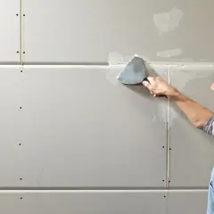 Mann spachtelt Rigipsplatten, um eine glatte Wand zu schaffen.