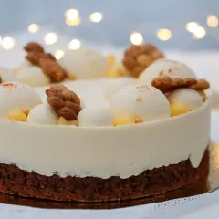 En vacker tårta med lemoncurd och chokladmousse, dekorerad med vita bollar, kex och gul topping. Bakgrunden har julbelysning.