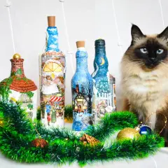 Urocze butelki ozdobione techniką decoupage na szkle, z zimowymi scenkami. Obok siedzi piękny kot.