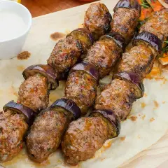 Kofta kebab z bakłażanem na patyku, podany na chlebku z sosem.