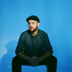 Matt Simons, nach dem Erdrutsch, sitzt nachdenklich vor blauem Hintergrund.
