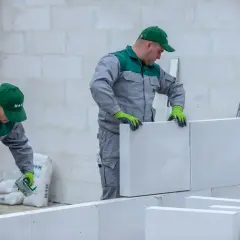 Pracownicy budowlani kontynuują murowanie ścian z bloczków, mimo ryzyka nocnych przymrozków. Szybkie tempo prac jest kluczowe.