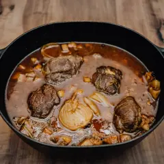 Herzhafte schmorgerichte im gusseisentopf, mit zarten Fleischrollen und Wurzelgemüse in einer dunklen Sauce.