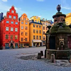 Färgglada hus i Gamla Stan, Stockholm, med en gammal fontän på kullerstensbelagd plats.