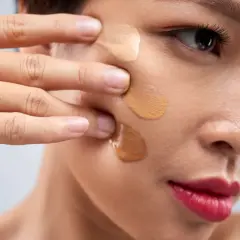 Dita sfumano campioni di fondotinta sul viso, mostrando a cosa serve il fondotinta per uniformare l'incarnato e coprire le imperfezioni.