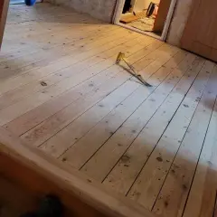 Ett rum med nylagt råspont golv. Ett verktyg ligger på golvet, redo för nästa steg i renoveringen.