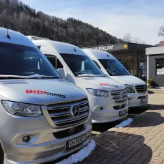 Trzy białe busy marki Mercedes stojące pod zadaszeniem stacji paliw.