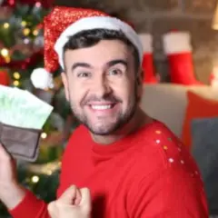 Hombre con gorro de Papá Noel muestra billetera llena de dinero, como si soñara que le toca la lotería en Navidad.