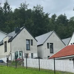 Nowe domy w stylu skandic hus, w budowie, z koparką na placu. W tle las.