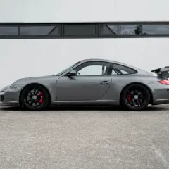 Grauer Porsche 997 GT3 RS mit schwarzem Flügel und roten Bremssätteln steht vor einer weißen Wand.
