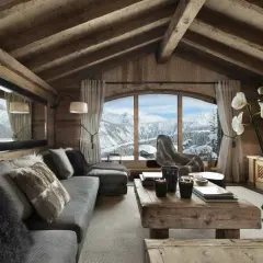 Gemütliches Wohnzimmer mit rustikaler Holzwand und Decke, einem großen Fenster mit Bergblick, einem Sofa mit Fellkissen und einem Holztisch. Luxus Chalet Inneneinrichtung.