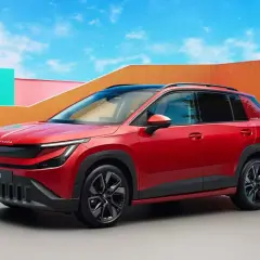 La Skoda Epiq rossa, un SUV compatto, si presenta con un design audace e moderno, circondata da un'architettura colorata e un cielo azzurro.