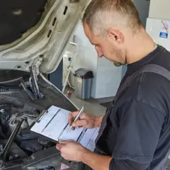 Mechanik spisuje stan techniczny pojazdu na karcie naprawy. W tle widać akumulatory.