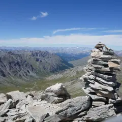 Un cairn, tel un tour du pain de sucre, domine un paysage de montagnes majestueuses sous un ciel bleu.
