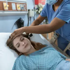 Pielęgniarka bada ucho pacjentki leżącej w łóżku szpitalnym.