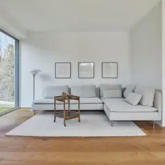 Großes Fenster mit Blick ins Grüne, ein bequemes Ecksofa, ein Beistelltisch und ein Lautsprecher prägen diese moderne Einrichtung.