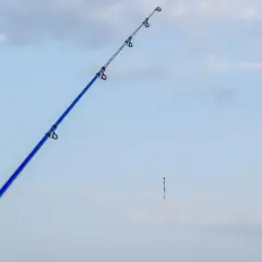 Błękitna wędka z cienką żyłką, na której wisi mały spławik. Czekam na branie, zastanawiając się, jaka żyłka na spławik będzie najlepsza.