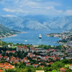 Vacker vy över Kotorbukten i Montenegro. Ett kryssningsfartyg ligger för ankar i det blå vattnet, omgivet av berg och en stad med röda tak. Montenegro mat kan avnjutas med en sådan här utsikt.