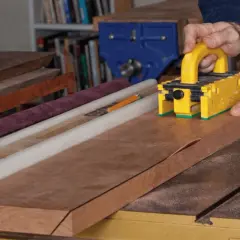 Maintenant, je vais fabriquer une scie sur table. Un artisan utilise un poussoir jaune pour guider une planche de bois sur la scie.