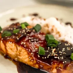 En saftig asiatisk lax med glansig teriyakisås, toppad med sesamfrön och salladslök, serveras med ris.