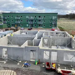 Grunden till ett hus byggs med prefabricerade betongelement. I bakgrunden syns gröna flerfamiljshus.